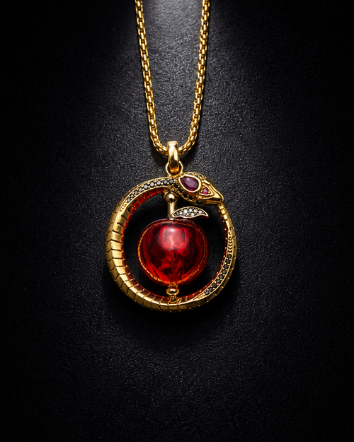A gold pendant necklace featuring a coiled snake around a red apple with a small purple eye detail, displayed on a dark textured background.